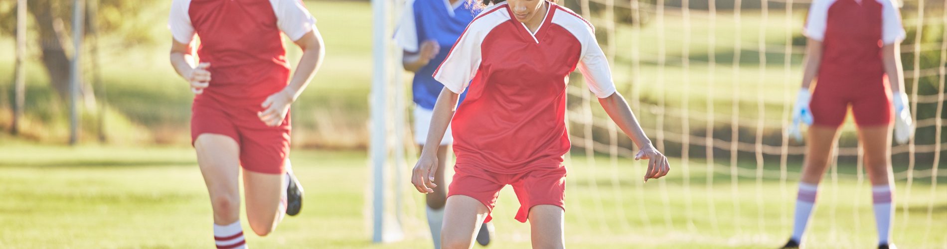 Una ragazza in maglia rossa arriva sul pallone durante una partita in un camp di calcio per ragazze