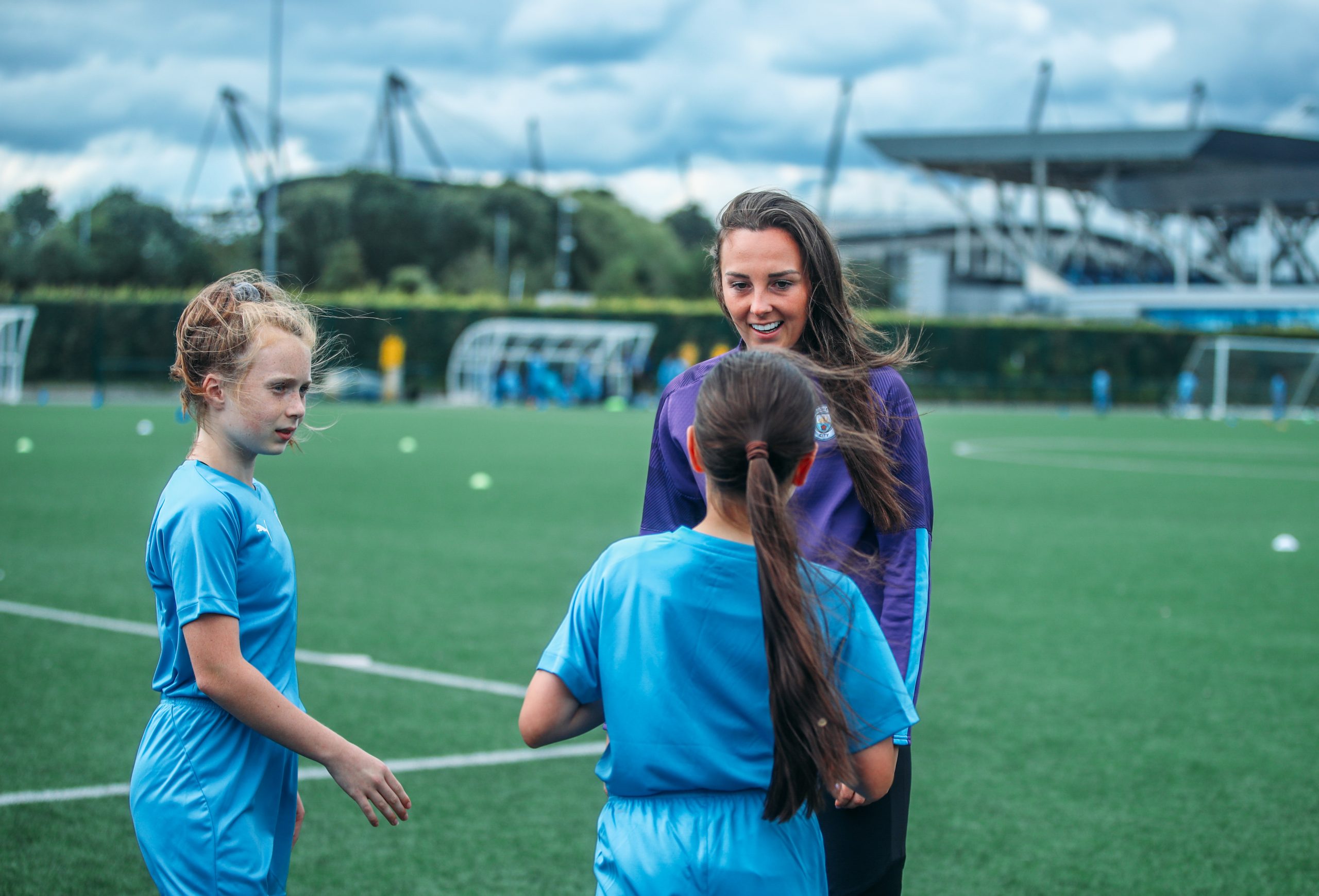 A female coach talking to two young players at a girls football camp